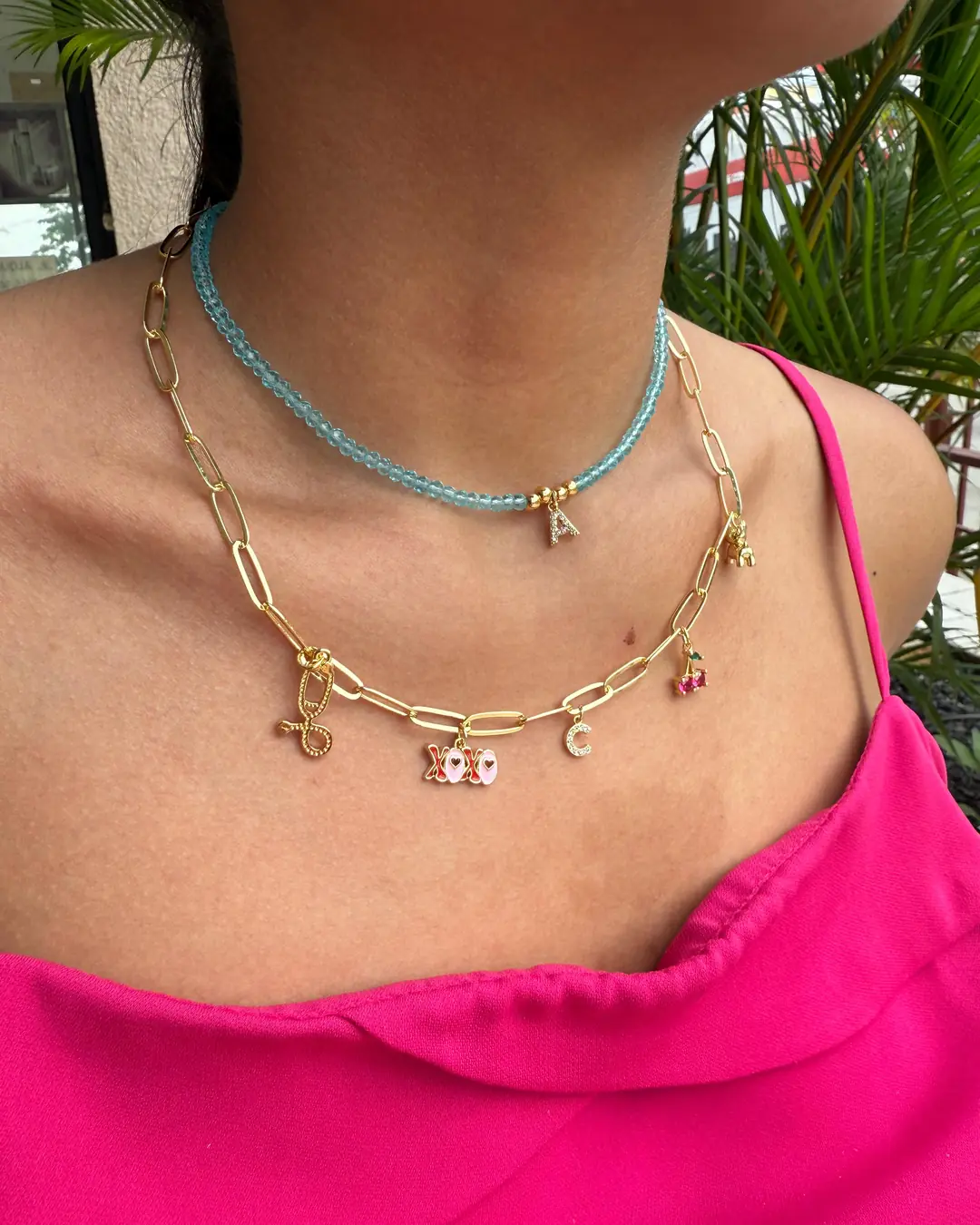 Charm Bar de The Luxury Minerals, foto 14: primer plano de collar de charms dorados sobre top fucsia
