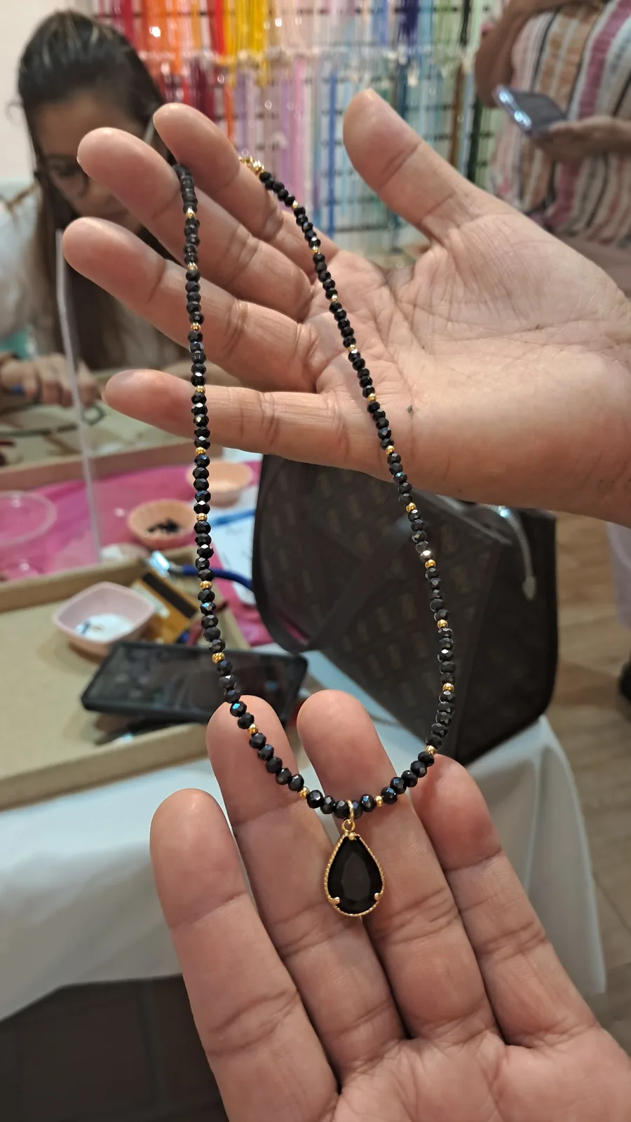 Choker Party de The Luxury Minerals, foto 4: manos sosteniendo un choker negro de mostacillas con dije de gota armado en la Choker Party